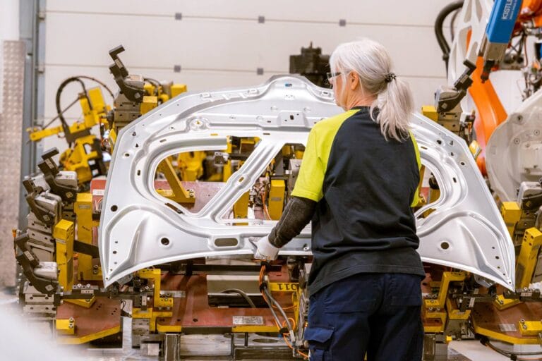 Medarbetare på EBP i Olofström arbetar med montering bilindustri, där en karossdel i stål hanteras i en automatiserad produktionslinje för fordonsindustrin.